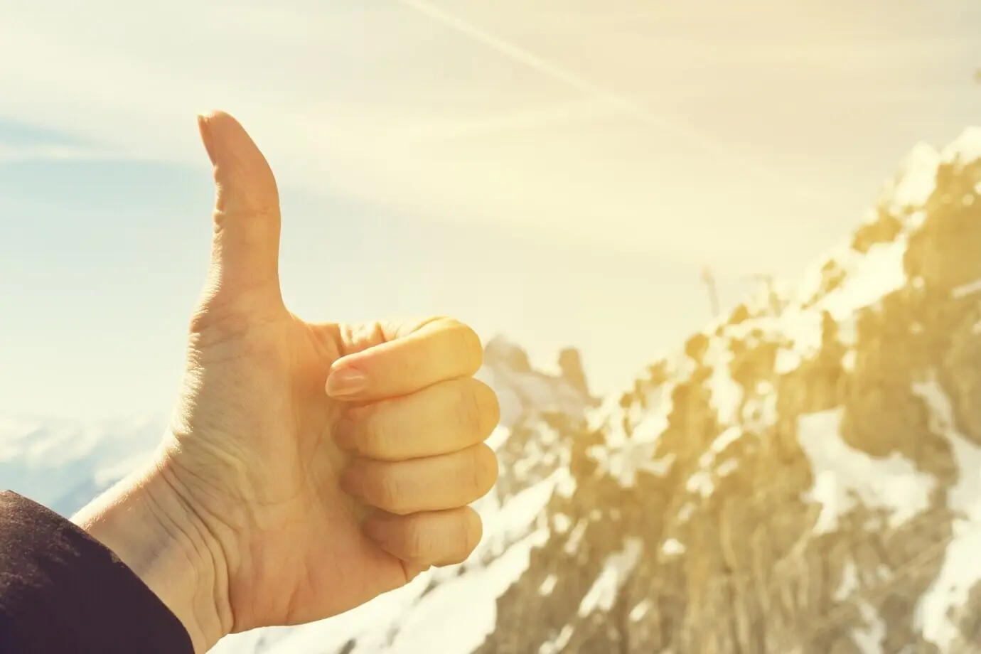 Концепция путешествий. Жест «палец вверх» на фоне природы. На заднем плане — размытые горы и красивое небо.