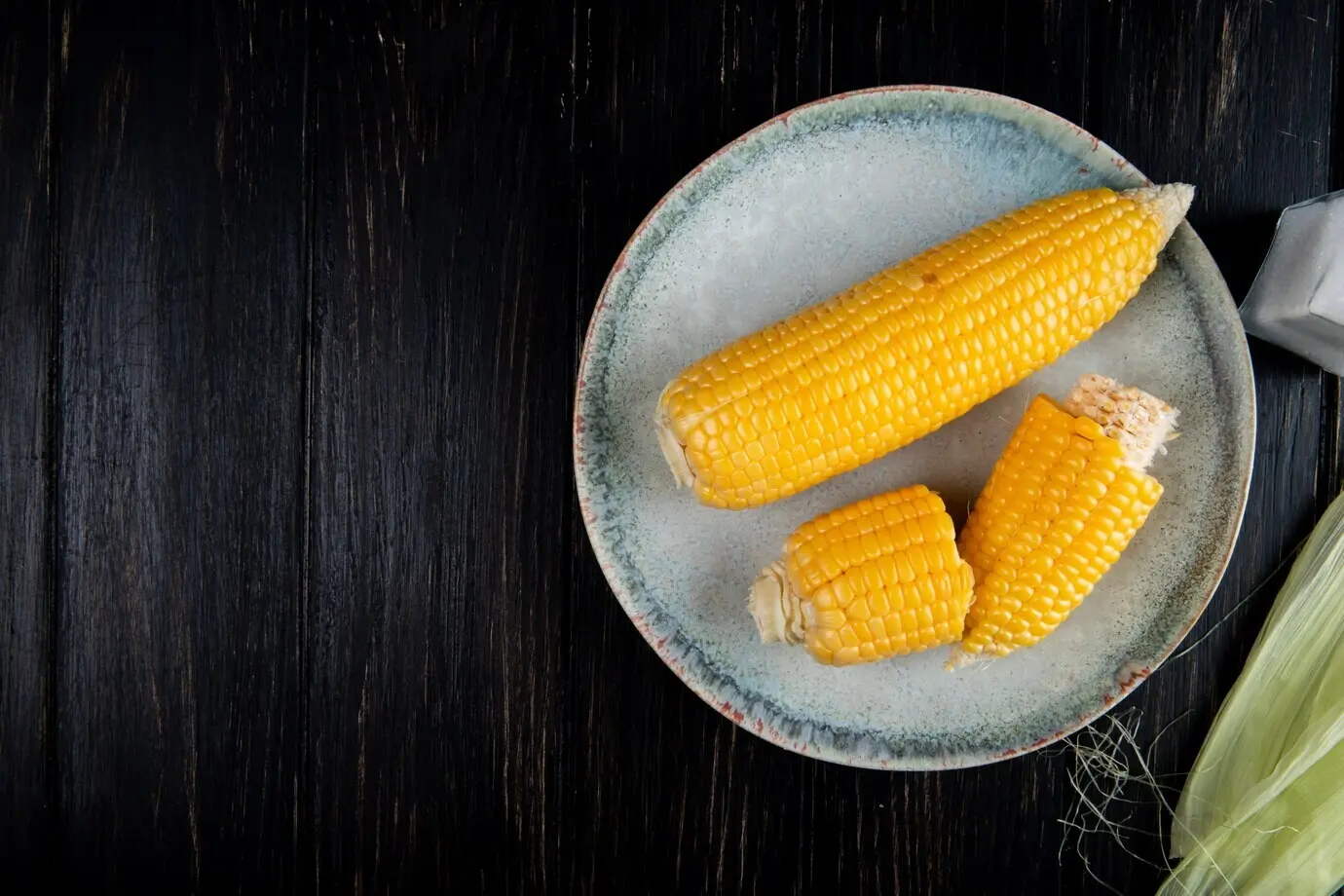 Крупный план приготовленных целых и нарезанных кукурузных початков справа на черном фоне с местом для текста.
